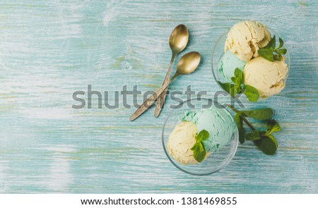 Mint and lemon ice cream with mint leaves in glass bowl on green wooden background. Space for text. Top view.