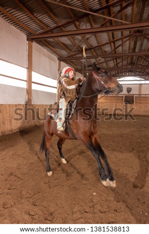 girl in clothes and a headdress of a native americans riding a horse in a pen in an arena