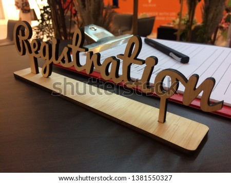 Laser cut wood wording 'REGISTRATION' with paper and pen on table