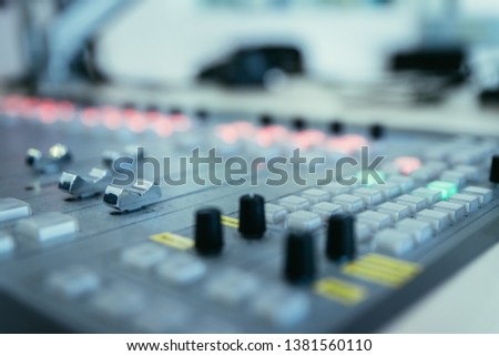 Close up picture of a soundboard in a broadcasting studio, computers in the blurry background