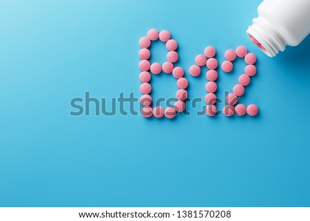 Pink pills in the shape of the letter B12 on a blue background, spilled out of a white can. Royalty-Free Stock Photo #1381570208
