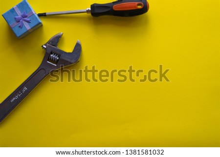 Adjustable wrench screwdriver and gift box lie on a yellow background