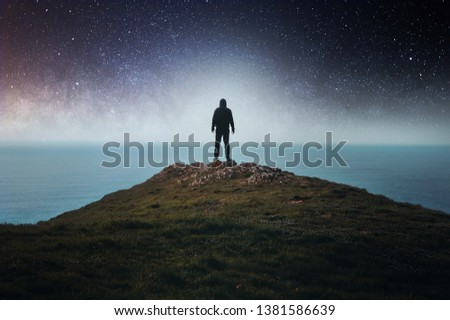 A concept of a hooded figure standing on a hill looking out to sea, with stars and the universe above.