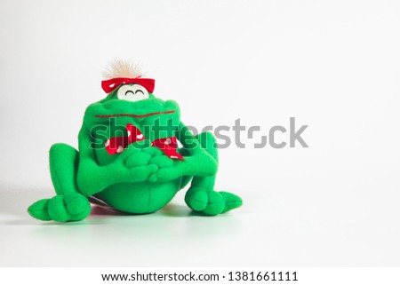 Happy green frog doll on color background. Isolated, green, red, white.