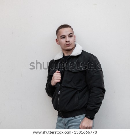 Nice cool modern young man in trendy seasonal clothes relaxes by standing near a vintage wall outdoors on a spring day. European handsome guy is resting. Beautiful stylish people.