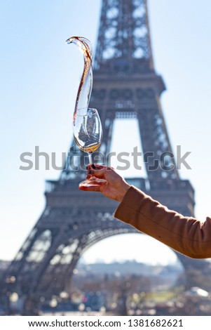France, Paris, Eiffel tower. Young girl is holding a glass of rose wine in her hand. Wine is pouring from the glass as flame. Historical building on background