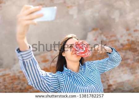 Young female with lollipop making selfie. Girl having fun outside. Young Woman smiling and making selfie at sunny summer day.