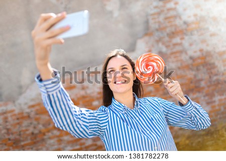 Young female with lollipop making selfie. Girl having fun outside. Young Woman smiling and making selfie at sunny summer day.