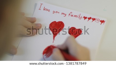 Children's hands write with a marker on a white sheet. I love you my family! Red heart.