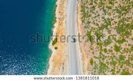 DRONE, TOP DOWN: Gray car driving down the scenic coastal road on a sunny summer day in Lefkas. Tourists on a fun road trip exploring the picturesque island in glistening deep blue Mediterranean sea. Royalty-Free Stock Photo #1381811018