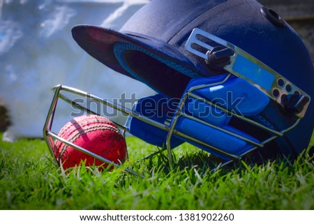 Cricket halmet and a ball on a green grass. Helmet protects batsman from fast balls which may otherwise cause harm to playing person.
