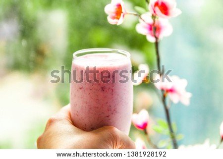 A close up of hand holding a pink milkshake cocktail on the green sunny background