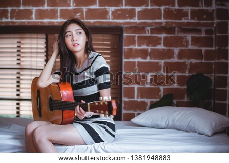 Young beautiful Asian woman is playing acoustic guitar on the bed at her bedroom, vintage warm tone