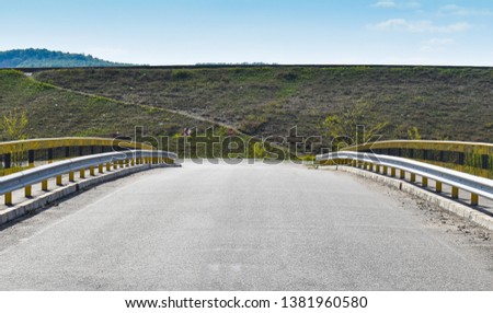 Symmetric picture along the empty bridge on the asphalt road.