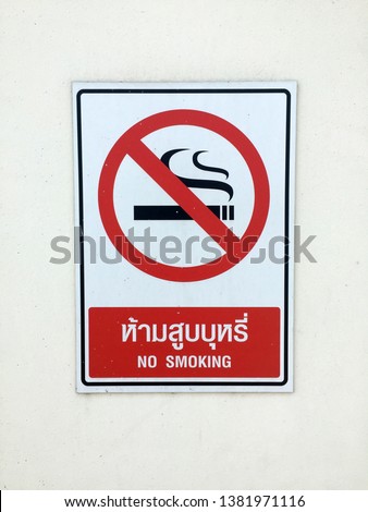 Sigh symbol of No Smoking in red black and white color with text in English and Thai on the wall.