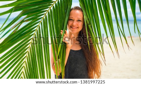 Happy girl with palm leaves on white sand beach