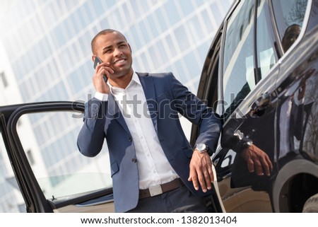 Young african american businessman standing near car talking on smartphone smiling cheerful