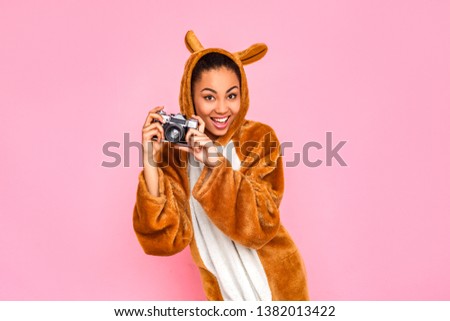 Young woman in bunny kigurumi standing isolated on pink background holdign film camera taking photos smiling playful