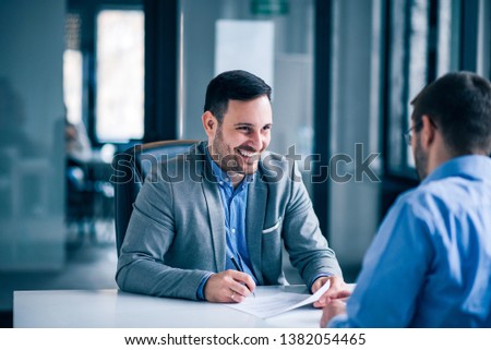 Handsome male client signing document on a meeting with real estate agent. Royalty-Free Stock Photo #1382054465