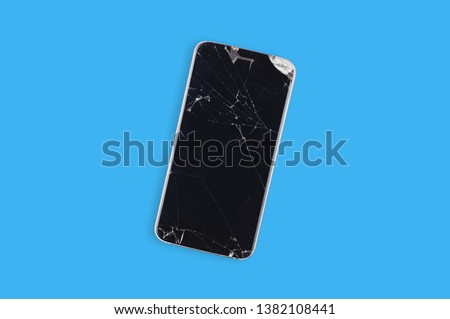 Black crashed smartphone with broken screen and body on blue table in service. Top view. Repair concept