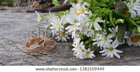 Two golden wedding rings with a beautiful bouquet of field flowers set on a wooden texture with natural day lighting