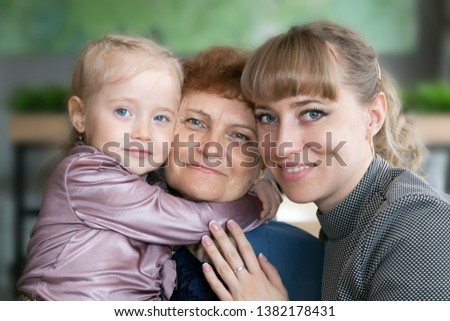 Daughter and granddaughter hug and kiss grandmother. A little girl and  young woman hug their elderly mom and grandmother tightly.