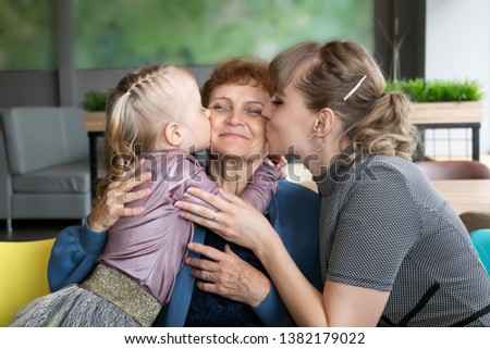 Daughter and granddaughter hug and kiss grandmother. A little girl and a young woman hug their elderly mom and grandmother tightly.