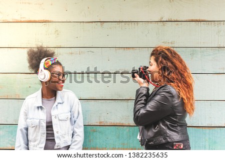Two Latin American Girls Taking Pictures to Each Other Outdoors. Friend Teenage Girls Using a Vintage Camera Over a Blue Wall. Youth Concept.