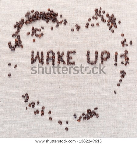 Wake up sign inside a heart made from roasted coffee beans shot top view on linea canvas aligned in the center.