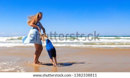 Mother and daughter are spinning and having fun on the beach at sunny day. 