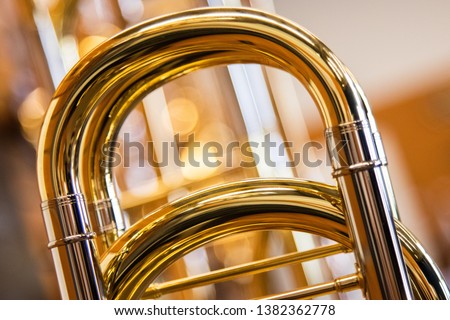 A close up shot of the main tuning slide of a Professional Bass Trombone with a line of trombones in the background out of focus with a bokeh background. Very warm tones of brass. Royalty-Free Stock Photo #1382362778