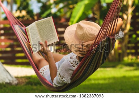 Woman with hat reading book in colorful hammock in tropical garden while relaxing in vacation. Royalty-Free Stock Photo #1382387093