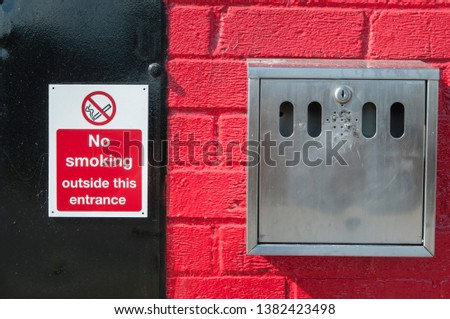 Sign warning people not to smoke outside an entrance, but making it convenient to do so, by placing an outside ashtray