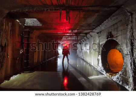 Silhouette of a man standing in the rays of light deep underground in a concrete tunnel. with red backlight. City dungeons. Underground city.