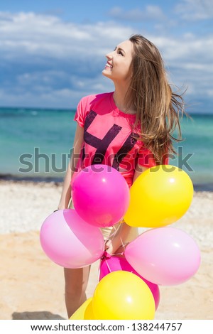 Happy girl holding bunch of colorful air balloons at the beach