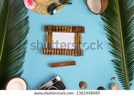 Stylish summer composition with photo frame, green leaves, hat and sunglasses on a blue pastel background. Artwork mockup with copy space