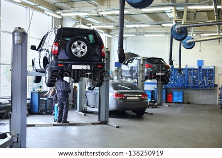 Three black cars stand in small service station and two men repair one car. Royalty-Free Stock Photo #138250919