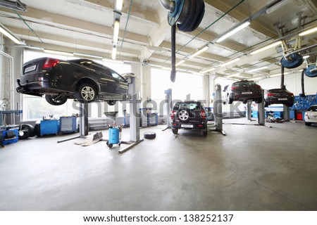 Four cars on lifts and on floor in small service station. Cars prepared to diagnosis and repair. Royalty-Free Stock Photo #138252137