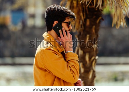 Fashion businessman with cellphone walking in city center near the river close a palm tree