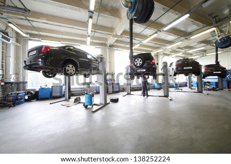 Four black cars on lifts in small service station and two men repair one car. Royalty-Free Stock Photo #138252224