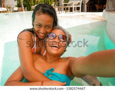 lifestyle outdoors portrait of Asian girlfriends enjoying Summer holidays at tropical beach resort swimming pool taking selfie photo with mobile phone playing together laughing and having fun