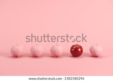 Outstanding red apple among pink painted apples on pastel pink background. Minimal fruit idea concept.