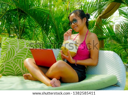 lifestyle outdoors portrait of young happy and attractive Asian Indonesian teenager girl in bikini networking with laptop computer at tropical resort garden bed enjoying holidays relaxed
