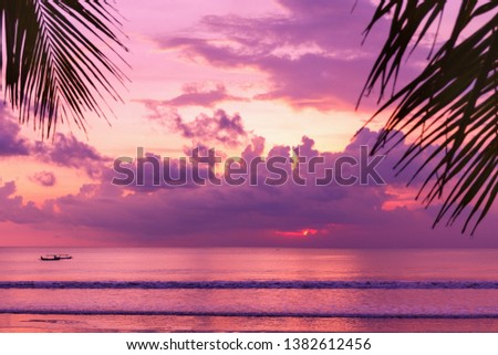 Purple sunset on the beach. View of the shore through palm leaves. Fantastic colorful landscape. Picturesque view. Color in nature. Bali, Kuta.
