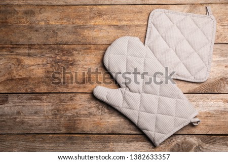 Protective oven glove and potholder on wooden table, top view with space for text Royalty-Free Stock Photo #1382633357