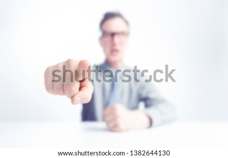 Businessman sitting at the table points a finger at you, shallow depth of field. Concept of evil boss. 