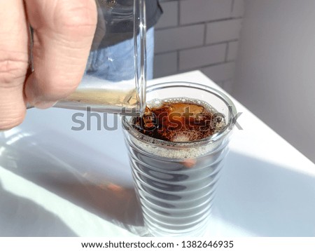 Pouring iced black coffee to the glass.