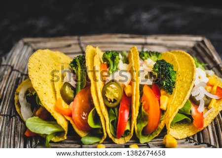 mexican cuisine, fresh corn tacos with colorful vegetables and white garlic sauce, on a plate of woven twigs on a dark, stone table decorated with jute
