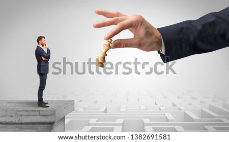 Little businessman from the top of the labyrinth fixing long term plan with big hand and chessman concept