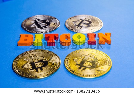 word bitcoin written with colored wooden letters with golden and silver bitcoins on blue background